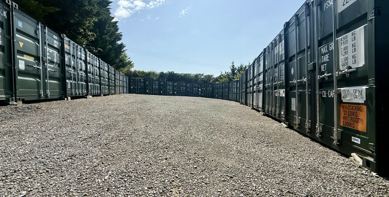 Two rows of green steel storage containers lining a gravelled avenue at Perry Storage's yard near Bath